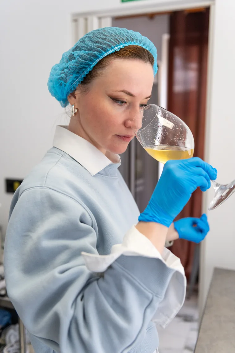 Ioana, fondatoarea Voyage Kombucha, mirosind un pahar de kombucha proaspăt fermentată în atelierul ei